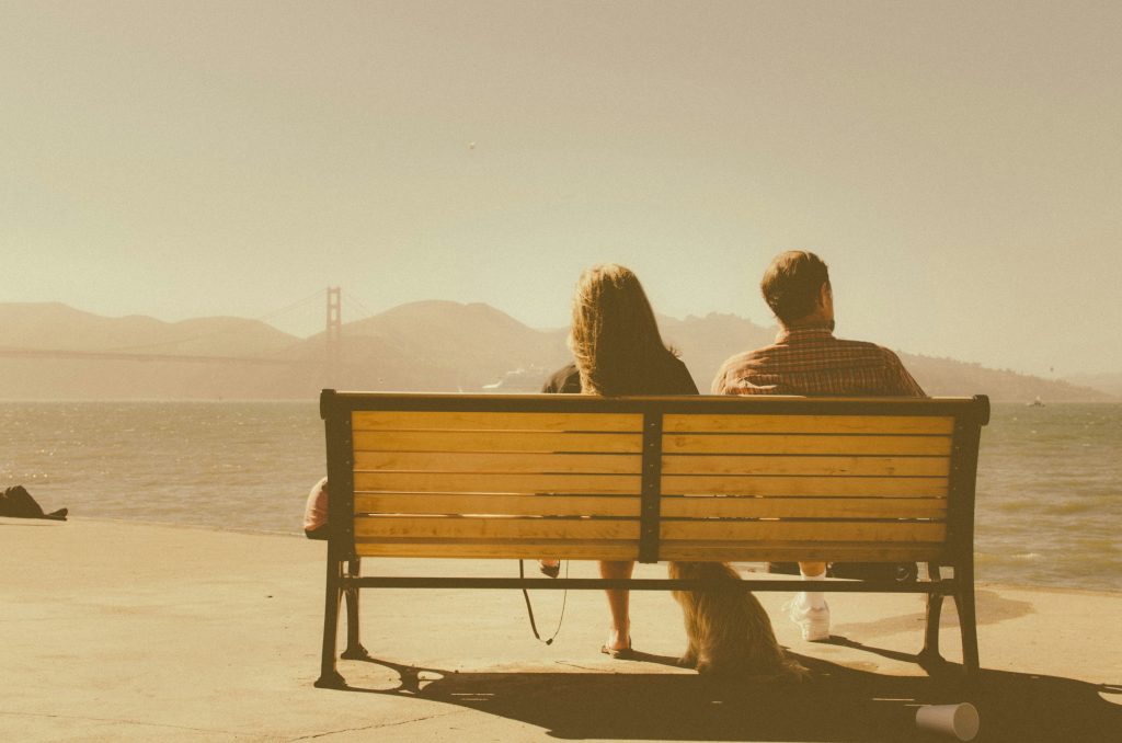 Pareja sentada en un banco mirando al mar, imagen de reflexión y conexión emocional en la terapia de pareja